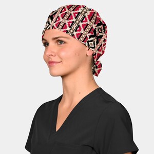 May include: A patterned surgical scrub cap featuring a geometric design in red, black, and cream colors. The cap is tied at the back and is worn by a person wearing a black scrub top.