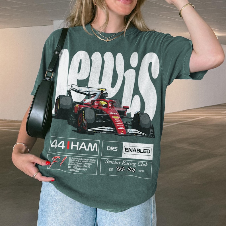 Pode incluir: T-shirt verde com um gr&aacute;fico de carro de corrida vermelho e preto e a palavra "LEWIS" em branco. A camisa tamb&eacute;m exibe "44 HAM DRS ENABLED" e "Sunday Racing Club EST 1950".