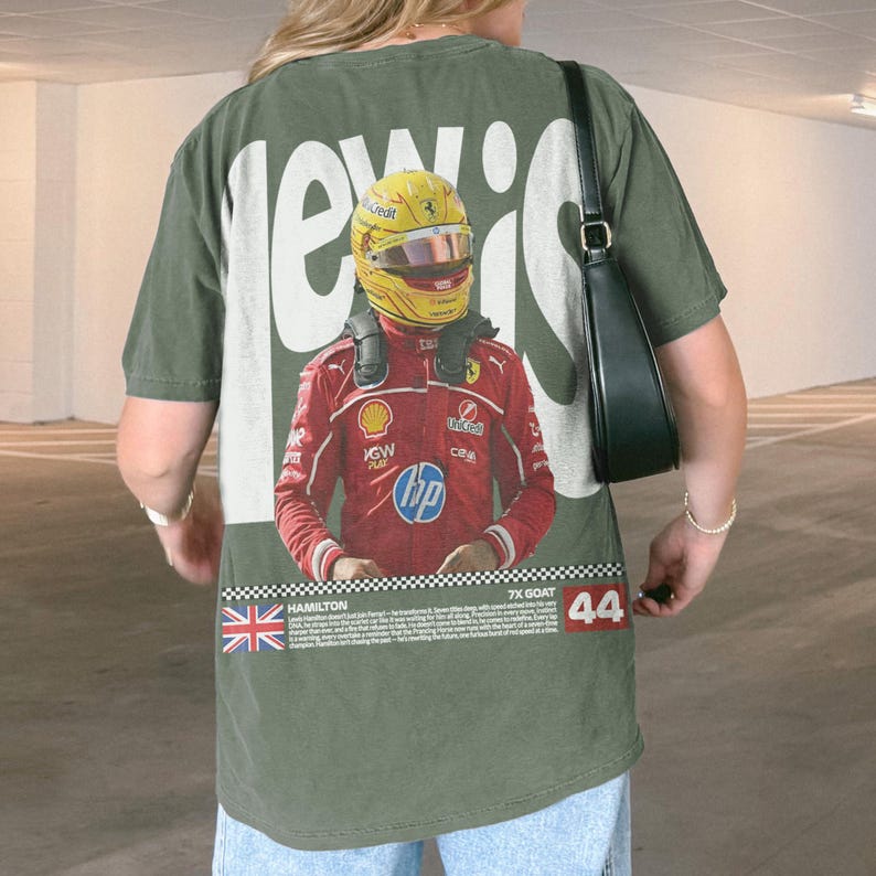 May include: Olive green t-shirt with a graphic of a Formula 1 driver in a red racing suit and yellow helmet. The text "LEWIS" is printed in white, with the number "44" and the words "7X GOAT" also visible.