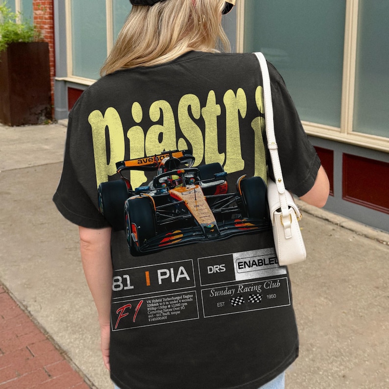 May include: Black t-shirt featuring a Formula 1 race car graphic with the name "Piastri" in yellow lettering. The shirt includes the number "81" and text that reads "Sunday Racing Club".