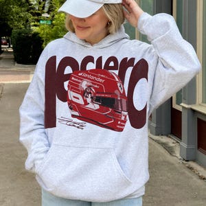 May include: A light gray hoodie with a large maroon graphic that says "Racer" and a red racing helmet. The helmet has sponsor logos and a signature. The hoodie has a front pocket and a drawstring hood.