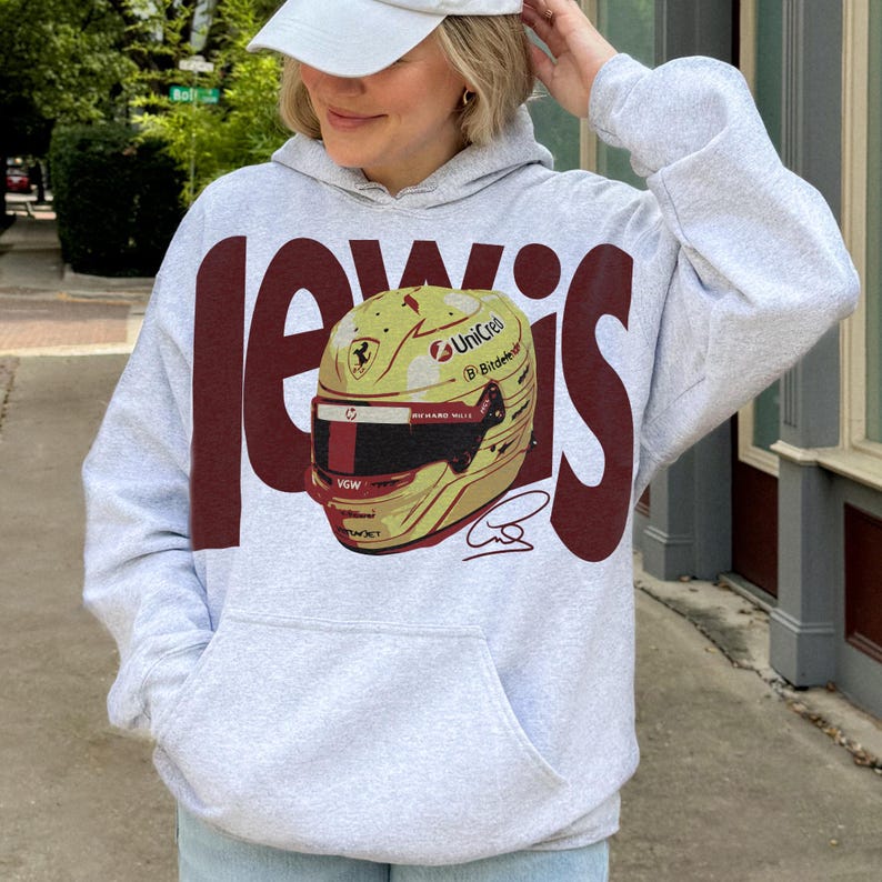 May include: A light gray hoodie with a large maroon "Lewis" graphic. The graphic features a yellow and gold racing helmet with sponsor logos and a signature. The hoodie has a front pocket and a drawstring hood.