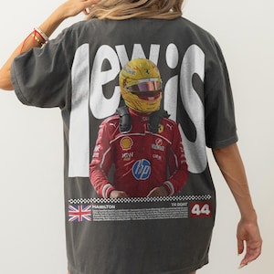 May include: Dark grey t-shirt with a graphic of a Formula 1 driver in a red racing suit and yellow helmet. The word "LEWIS" is printed in large white letters above the image. The number "44" is printed in red.