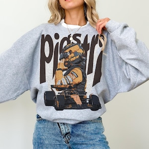 K&ouml;nnte beinhalten: Ein graues Sweatshirt mit einem Aufdruck eines Rennfahrers in Helm und Rennanzug. Das Wort "Piers" ist in gro&szlig;en, dunkelbraunen Buchstaben oben aufgedruckt. Das Sweatshirt hat lange &Auml;rmel und einen Rundhalsausschnitt.