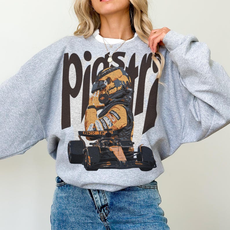 K&ouml;nnte beinhalten: Ein graues Sweatshirt mit einem Aufdruck eines Rennfahrers in Helm und Rennanzug. Das Wort "Piers" ist in gro&szlig;en, dunkelbraunen Buchstaben oben aufgedruckt. Das Sweatshirt hat lange &Auml;rmel und einen Rundhalsausschnitt.
