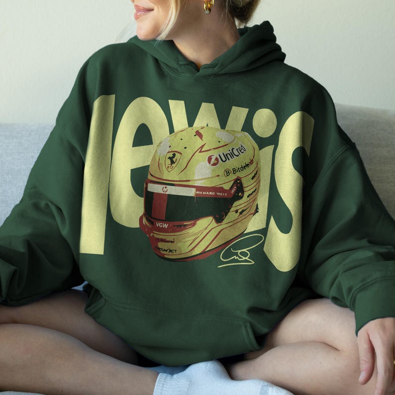 May include: A dark green hoodie with the name "LEWIS" in large yellow letters. The hoodie features a yellow and red racing helmet graphic with sponsor logos and a signature. The hoodie is made of a soft material.