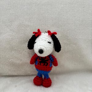 May include: A handmade crochet Snoopy doll dressed as Spider-Man. The doll features a white head, black ears, and red bows. It wears a red and blue Spider-Man costume with a black spider emblem. The doll is approximately 4 inches tall.
