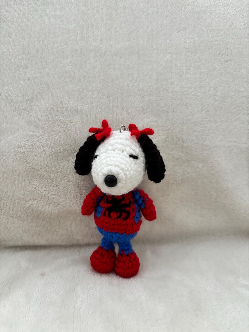 May include: A handmade crochet Snoopy doll dressed as Spider-Man. The doll features a white head, black ears, and red bows. It wears a red and blue Spider-Man costume with a black spider emblem. The doll is approximately 4 inches tall.