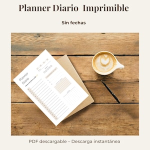 May include: A printable planner with the text "Planner Diario Imprimible" and "Sin fechas" on a wooden surface. A cup of coffee with latte art and a pen are also on the table. The planner is white with beige accents.