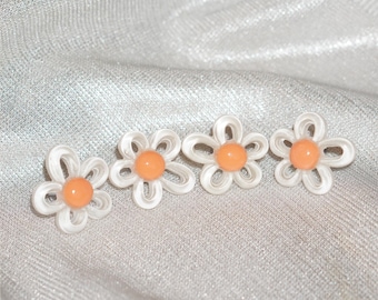 May include: Four daisy-shaped earrings with white petals and orange centers. The earrings are arranged in a row on a shiny, silver fabric. The floral design is simple and elegant, suitable for everyday wear.
