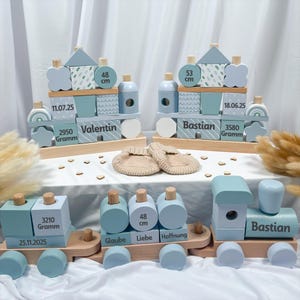 Könnte beinhalten: Holzspielzeug-Zugsets in Blau- und Naturholztönen, personalisiert mit Namen, Daten und Maßen. Enthält gestapelte Blockzüge und ein Paar beige Baby-Schuhe. Die Züge tragen die Namen "Valentin" und "Bastian".