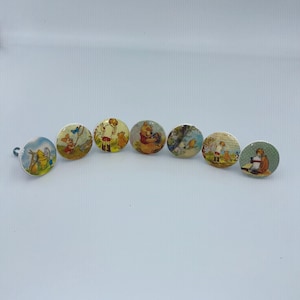May include: A set of seven round cabinet knobs featuring colourful illustrations of Winnie the Pooh characters. Each knob displays a different scene with Pooh, Piglet, and Christopher Robin in various outdoor settings, finished with a smooth surface.