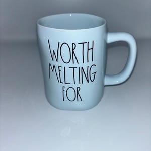 May include: A light blue ceramic mug with a rounded handle and a smooth finish. The front of the mug features the black text "WORTH MELTING FOR" written in a simple, thin, handwritten-style font centered on the body of the vessel.
