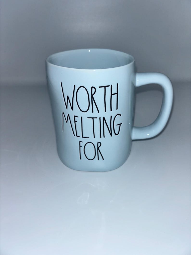 May include: A light blue ceramic mug with a rounded handle and a smooth finish. The front of the mug features the black text "WORTH MELTING FOR" written in a simple, thin, handwritten-style font centered on the body of the vessel.