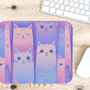 May include: A rectangular mousepad featuring a repeating pattern of stylized cat faces in shades of pink, blue, and purple. The cats have various expressions, with closed and open eyes. The mousepad is on a wooden desk next to a keyboard and mouse.