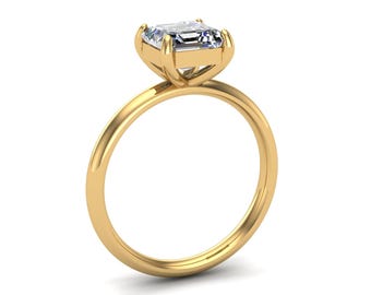 May include: A gold ring with a square-cut, clear gemstone. The ring has a thin band and a four-prong setting that holds the gemstone. The ring is set against a white background.
