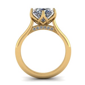 Puede incluir: Un anillo de compromiso de oro con una piedra preciosa grande y transparente. El anillo presenta un engaste único de inspiración floral y pequeñas piedras de acento. La banda es lisa y pulida.