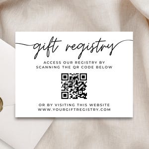 Pode incluir: Um cartão branco com as palavras "gift registry" em elegante escrita preta. Abaixo, lê-se "Access our registry by scanning the QR code below" e "Or by visiting this website www.yourgiftregistry.com". Um código QR está no centro.