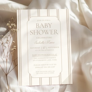 Puede incluir: Una invitación a un baby shower con fondo crema y rayas beige verticales. El texto dice "Únase a nosotros para un baby shower celebrando a Isabella Moore" con detalles del evento. Una ramita de flores secas está en primer plano.