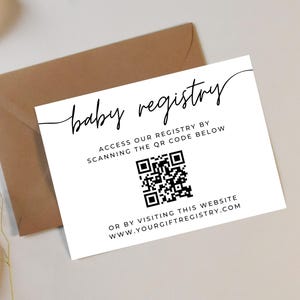 May include: A white baby registry card with black script and a QR code, placed on a beige surface next to a brown envelope. The card reads "baby registry" and provides instructions to access the registry via QR code or website.