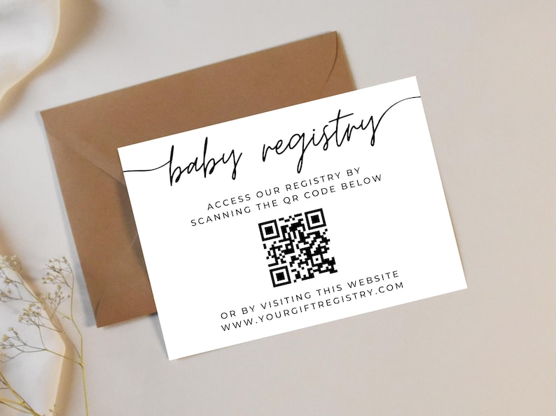 May include: A white baby registry card with black script and a QR code, placed on a beige surface next to a brown envelope. The card reads "baby registry" and provides instructions to access the registry via QR code or website.