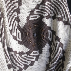 May include: A crocheted blanket with a circular design in brown and white. The centre of the blanket features a brown circle with a beaded border.