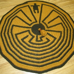 May include: A round crocheted rug with a brown and gold color scheme. The rug features a circular maze pattern with a tassel in the center.