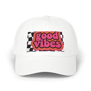 Può includere: Cappellino da baseball bianco con una toppa retrò. La toppa presenta le parole "good vibes" in rosa e arancione, su uno sfondo a scacchi bianco e nero. Un accessorio casual e classico.