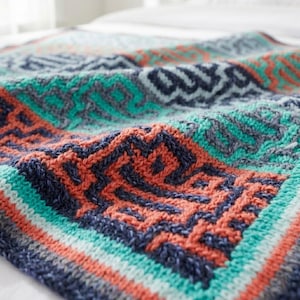 May include: A knitted blanket with a geometric pattern in shades of teal, coral, navy, and gray. The blanket features a repeating design with a border of stripes. The soft texture and vibrant colors create a cozy and inviting feel.