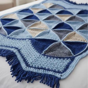 May include: A handmade crochet blanket in shades of blue, gray, and beige. The blanket features a geometric pattern of triangles and a fringed edge. The soft, textured blanket is perfect for adding warmth and style to any room.