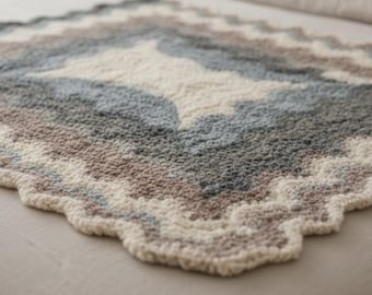 Pode incluir: Um cobertor feito à mão com um padrão geométrico. O cobertor apresenta um design de diamante em tons de creme, cinza, azul e marrom. As bordas têm uma borda ondulada. O cobertor é feito de material macio e felpudo.