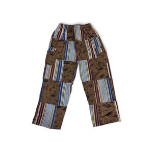 May include: Patchwork trousers featuring a brown fabric with a black mushroom and butterfly print, alternating with vertical panels of blue, white, and maroon striped fabric. The pants have an elasticated waistband and a straight-leg cut.