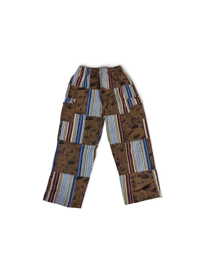 May include: Patchwork trousers featuring a brown fabric with a black mushroom and butterfly print, alternating with vertical panels of blue, white, and maroon striped fabric. The pants have an elasticated waistband and a straight-leg cut.