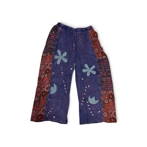 May include: Purple pants with an elastic waistband and drawstring. The front features light blue fabric flower appliqu&eacute;s with embroidered stems and leaves. The outer side panels are decorated with a dark red and brown circular pattern.
