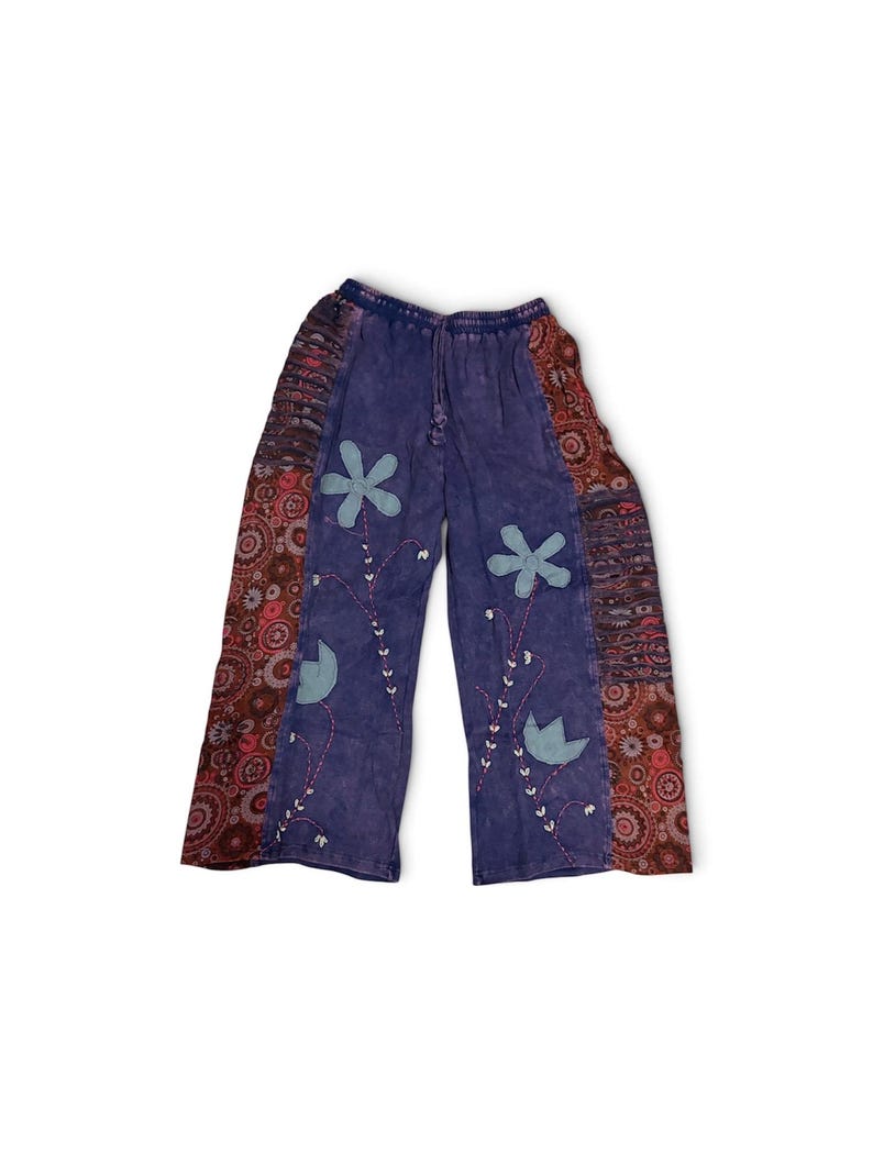 May include: Purple pants with an elastic waistband and drawstring. The front features light blue fabric flower appliqu&eacute;s with embroidered stems and leaves. The outer side panels are decorated with a dark red and brown circular pattern.