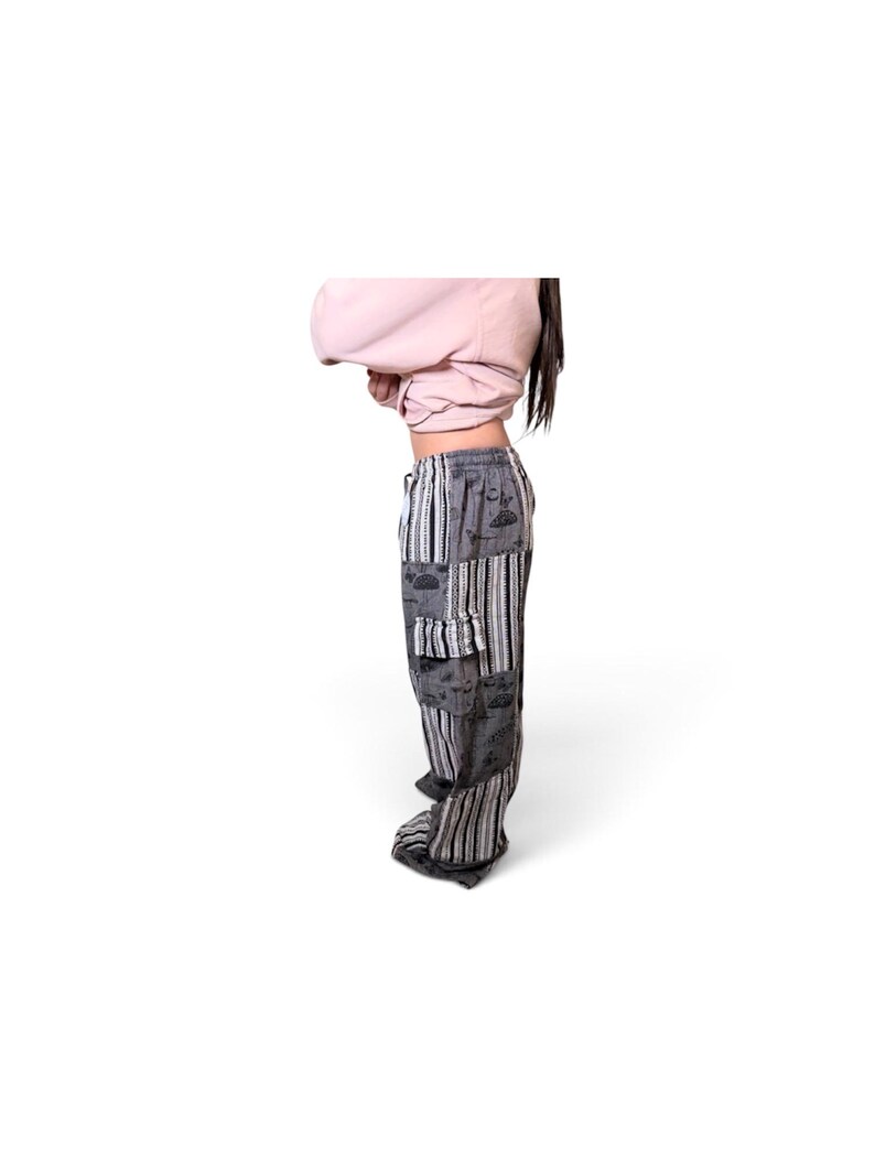 May include: Loose-fitting pants featuring a patchwork design of grey fabric with black and white line illustrations and vertical black and white striped panels. The pants include a side cargo pocket and an elastic waistband with a drawstring closure.