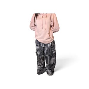 May include: A light pink hooded sweatshirt with a front kangaroo pocket and matching drawstrings, paired with loose-fitting cargo pants featuring a patchwork design of black and gray striped fabric and panels with a dark floral pattern.
