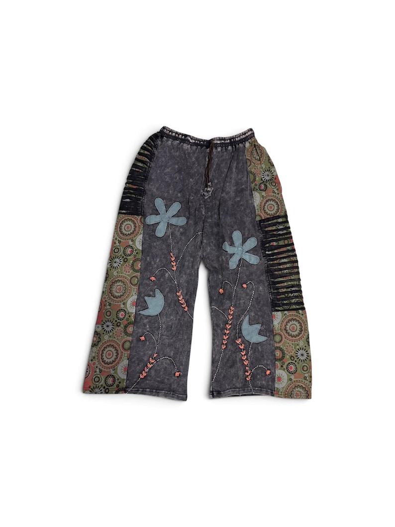 May include: Wide-leg pants in a dark gray acid-wash fabric featuring light blue fabric flower appliqu&eacute;s, embroidered stems with small pink accents, side panels with a multi-colored circular pattern, and black horizontal cut-out detailing.