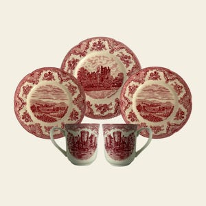 May include: A set of red and white ceramic dishes and mugs. The plates and mugs feature a scenic design of a castle and landscape. The plates have a scalloped edge and floral border. The mugs have a handle and a matching castle design.