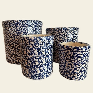 May include: Set of four ceramic planters with a speckled blue and white pattern. The planters are cylindrical with varying heights and diameters. The interior of each planter is a cream color.