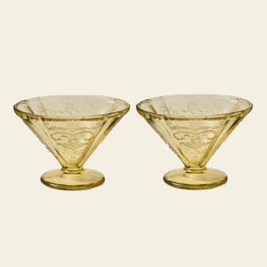 May include: Two yellow-tinted glass dessert dishes. Each dish has a conical bowl with etched floral designs and a rounded base. The dishes are likely vintage or antique, adding a touch of elegance to any table setting.