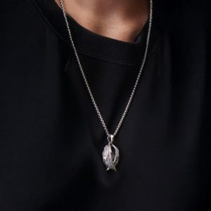 May include: Silver-toned pendant necklace featuring a detailed feather design. The pendant hangs from a delicate chain, creating a classic and elegant look. The necklace is worn against a black background.