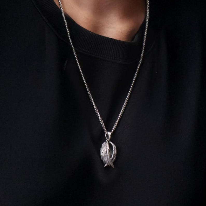 May include: Silver-toned pendant necklace featuring a detailed feather design. The pendant hangs from a delicate chain, creating a classic and elegant look. The necklace is worn against a black background.