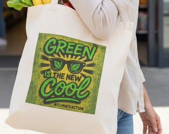 May include: A canvas tote bag with the text "GREEN IS THE NEW COOL" and sunglasses graphic. The bag is filled with groceries, including bananas, bread, and vegetables. The bag is carried by a person in front of a store.