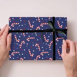 Könnte beinhalten: Ein verpacktes Geschenk mit marineblauem Hintergrund mit einem Muster aus weißen Sternen, roten Sternen und rot-weißen Zuckerstangen. Ein schwarzes Samtband und eine Schleife sichern das Geschenk.