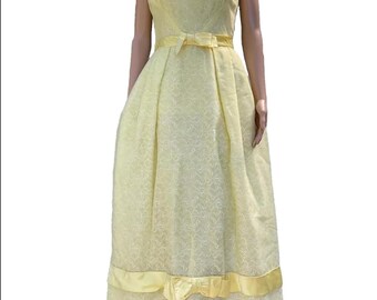 May include: A sleeveless, pale yellow vintage dress with a square neckline and a fitted bodice. The dress features a bow at the waist and a ribbon detail with a bow at the hem. The fabric has a subtle floral pattern, and the dress is displayed on a mannequin.