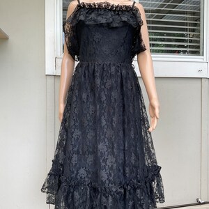 May include: A black lace dress with a ruffled neckline and hem. The dress has a fitted bodice and a flowing skirt.