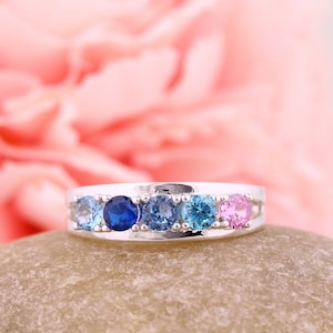 May include: A silver ring with five round gemstones. The gemstones are blue, light blue, and pink.
