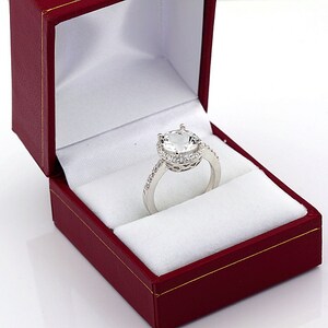 May include: A silver ring with a large, clear, round gemstone surrounded by a halo of smaller gemstones. The ring is in a red velvet ring box.