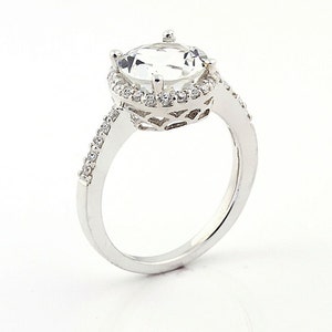 May include: A silver ring with a large, clear, round gemstone surrounded by a halo of smaller gemstones. The band is set with smaller gemstones.